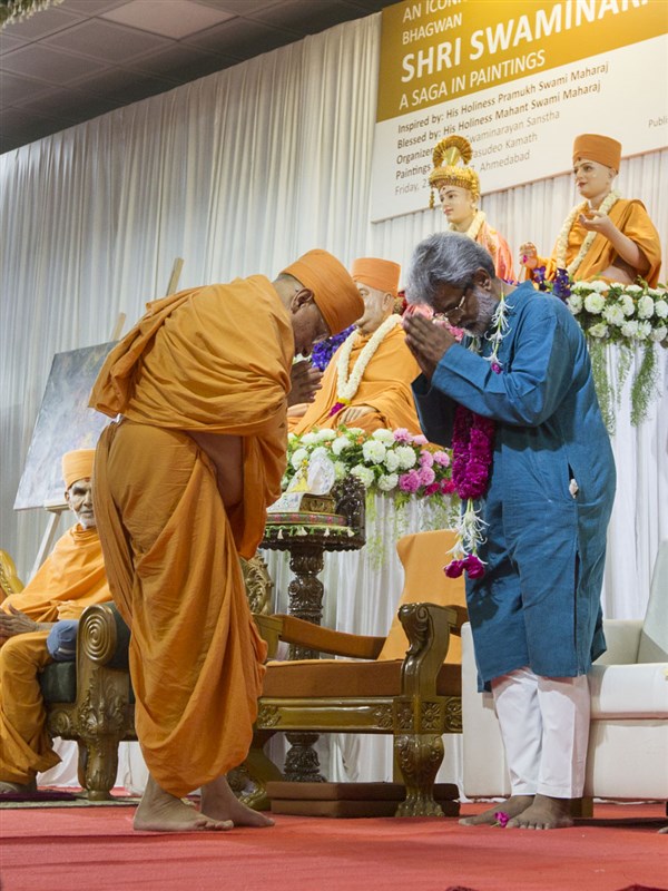 Pujya Ishwarcharan Swami honors Shri Vasudeo Kamath, the artist who painted all the paintings in the book, with a garland